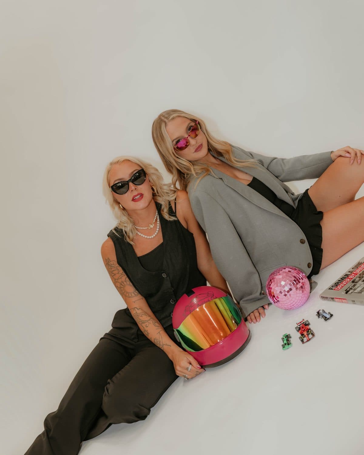 Jensen and Adri in sunglasses, lounging with the pink helmet, a pink disco ball, and toy F1 cars